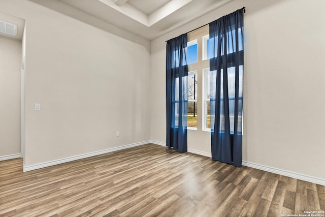 spare room with baseboards, visible vents, and wood finished floors