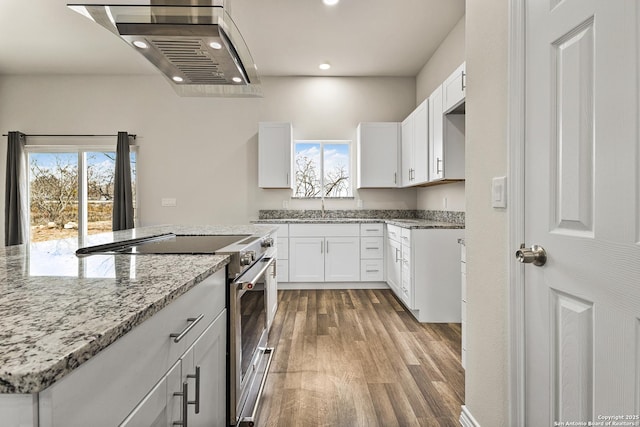 kitchen with wood finished floors, light stone countertops, extractor fan, stainless steel stove, and white cabinetry