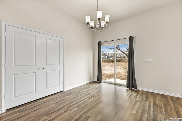 unfurnished dining area featuring dark wood-style floors, baseboards, and a notable chandelier