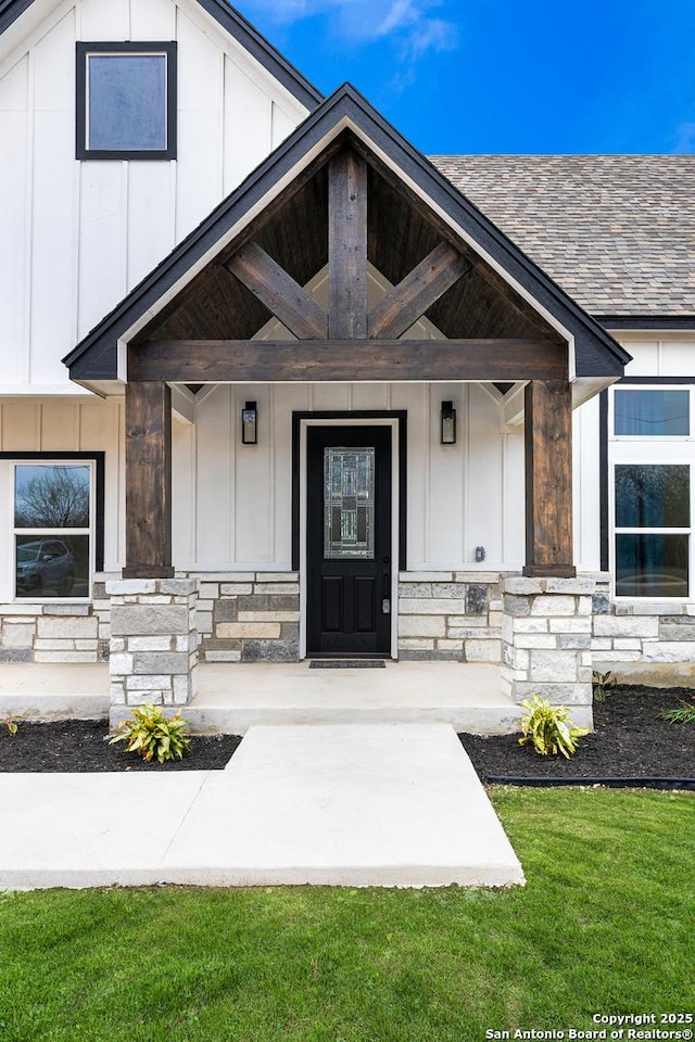 entrance to property with a yard, stone siding, a shingled roof, and board and batten siding