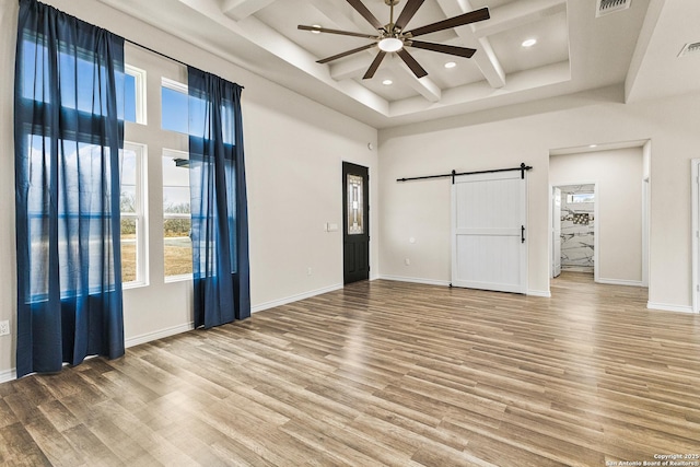 spare room with a barn door, wood finished floors, a towering ceiling, and a healthy amount of sunlight