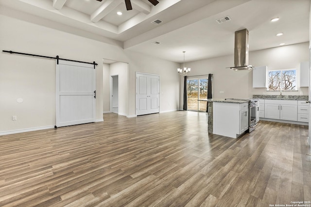 kitchen with a barn door, visible vents, white cabinets, island exhaust hood, and stainless steel stove