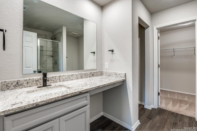 bathroom with baseboards, vanity, wood finished floors, a walk in closet, and a stall shower