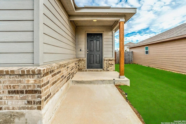 property entrance with fence, a yard, and brick siding