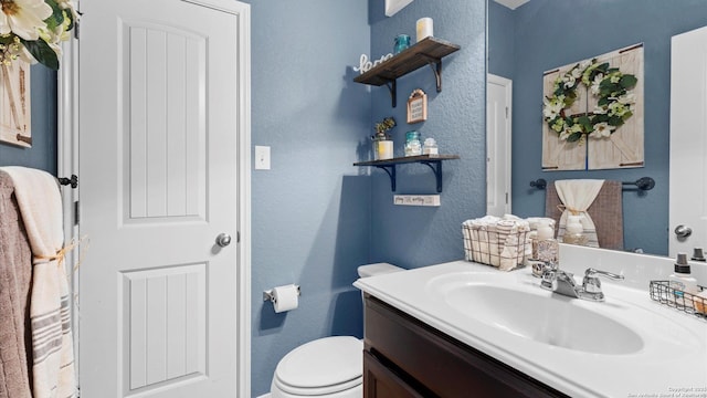 half bathroom featuring toilet, a textured wall, and vanity