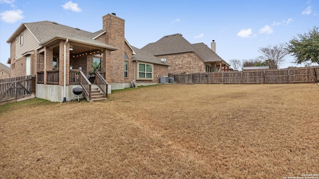 back of house with brick siding, a lawn, central AC, and a fenced backyard