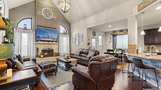 living room featuring a fireplace, high vaulted ceiling, dark wood finished floors, and a chandelier