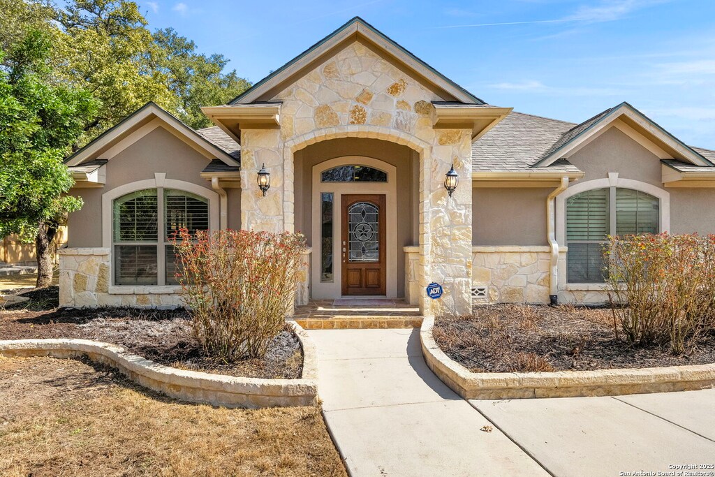 view of exterior entry featuring stucco siding, stone siding, and a shingled roof