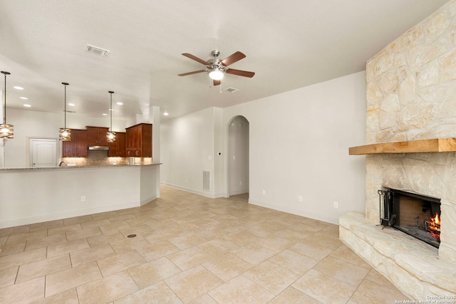 unfurnished living room with a fireplace, visible vents, a ceiling fan, and arched walkways