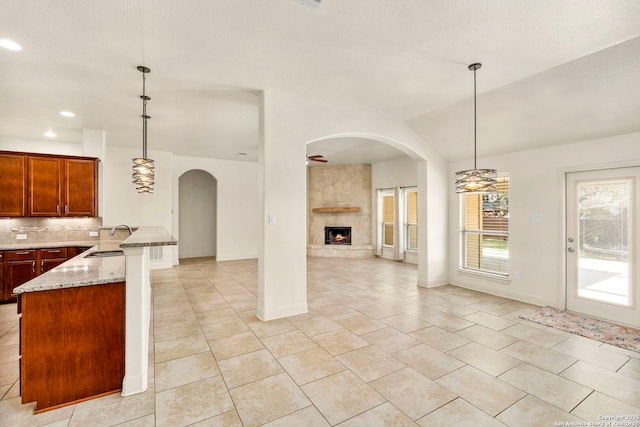 kitchen with hanging light fixtures, tasteful backsplash, a sink, light stone counters, and open floor plan