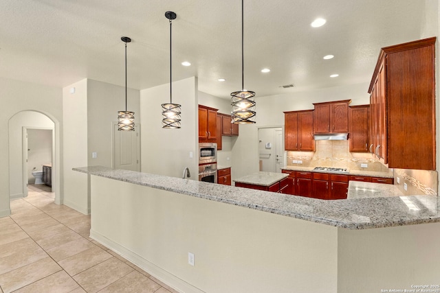 kitchen featuring decorative light fixtures, under cabinet range hood, stainless steel appliances, light stone countertops, and arched walkways