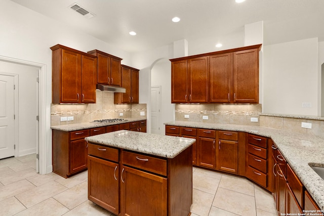 kitchen with under cabinet range hood, light tile patterned flooring, light stone counters, and visible vents