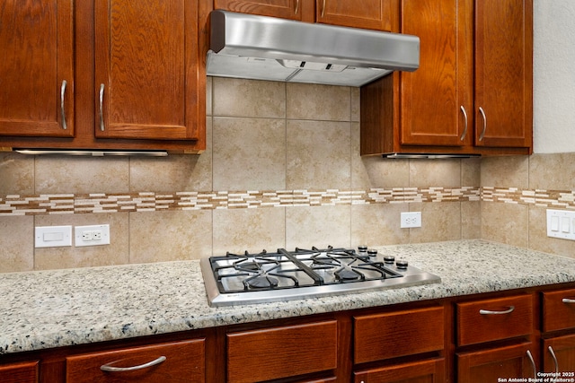 kitchen with backsplash, stainless steel gas cooktop, under cabinet range hood, and light stone countertops