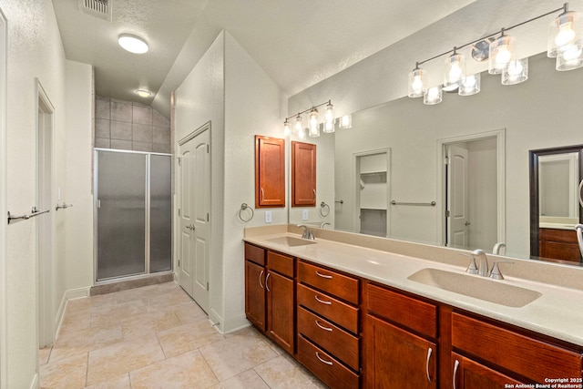 full bathroom with double vanity, a sink, a shower stall, and visible vents