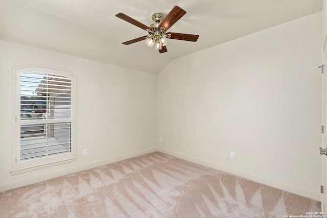 empty room featuring lofted ceiling, light carpet, baseboards, and a ceiling fan