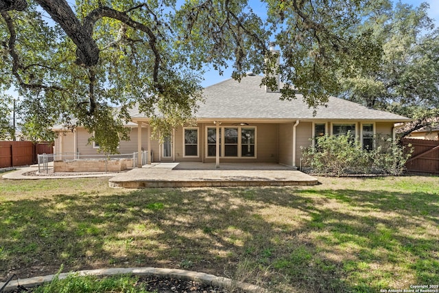 back of house featuring fence, a lawn, a patio, and a shingled roof