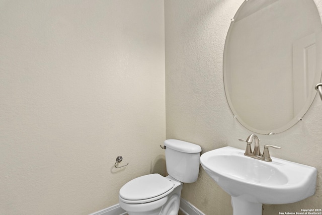 bathroom featuring baseboards, toilet, a sink, and a textured wall