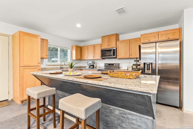 kitchen with a breakfast bar area, stainless steel appliances, a kitchen island, sink, and light stone countertops