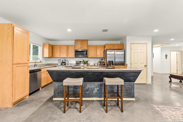 kitchen with appliances with stainless steel finishes, light brown cabinetry, a kitchen bar, a kitchen island, and sink