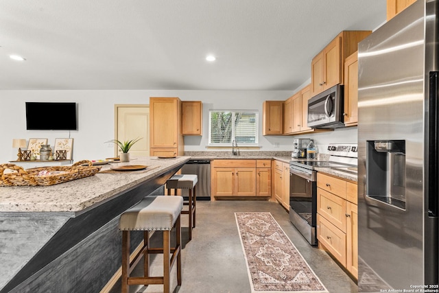 kitchen featuring stainless steel appliances, light brown cabinets, a kitchen bar, light stone counters, and sink