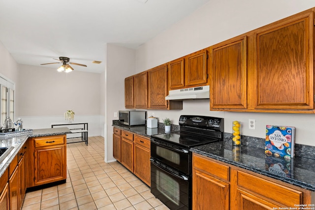 kitchen featuring stainless steel microwave, dark stone counters, under cabinet range hood, brown cabinetry, and range with two ovens