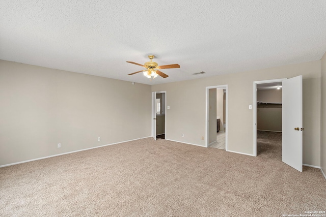 unfurnished bedroom featuring visible vents, a walk in closet, light carpet, a textured ceiling, and ceiling fan