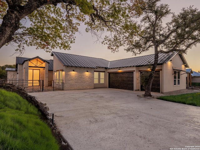 view of front of house with metal roof, concrete driveway, stone siding, a standing seam roof, and a garage