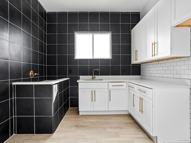 kitchen featuring light countertops, tile walls, white cabinets, a sink, and light wood finished floors