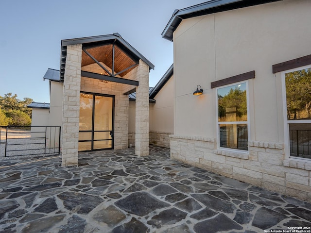 exterior space with metal roof, stucco siding, stone siding, and a patio