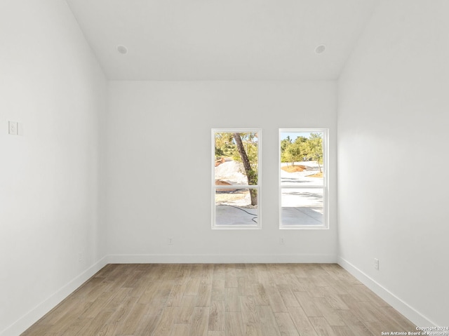 spare room with baseboards, lofted ceiling, and light wood-style flooring