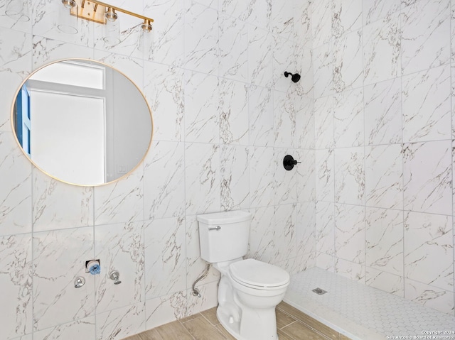 bathroom featuring tiled shower, toilet, and tile walls