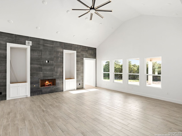 unfurnished living room featuring high vaulted ceiling, light wood finished floors, a tiled fireplace, and tile walls