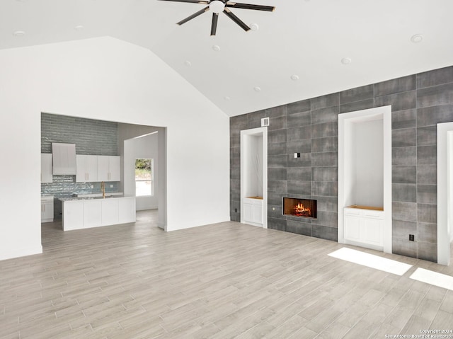 unfurnished living room with a sink, tile walls, light wood-type flooring, a ceiling fan, and a fireplace