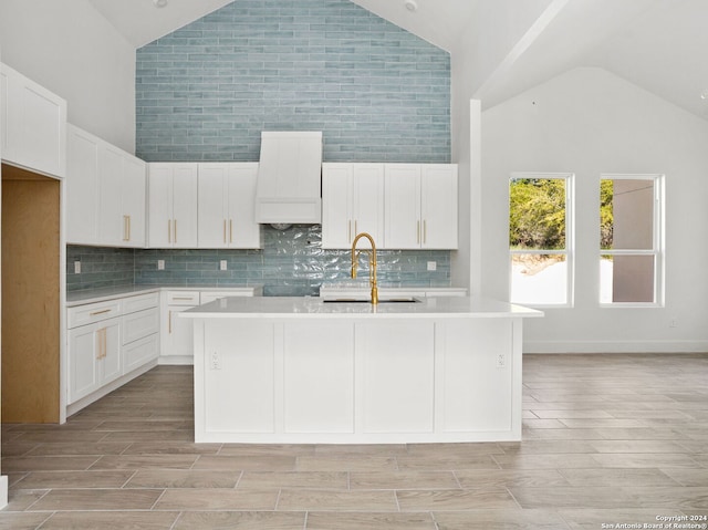 kitchen featuring high vaulted ceiling, an island with sink, white cabinetry, custom range hood, and light countertops