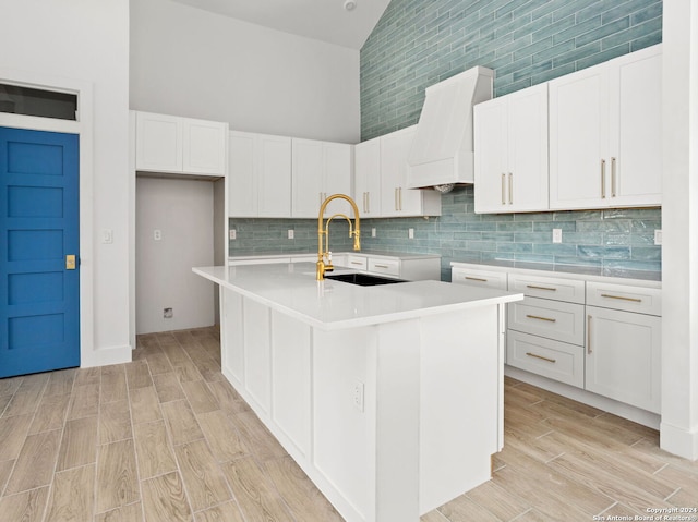 kitchen featuring light countertops, premium range hood, white cabinets, and a center island with sink