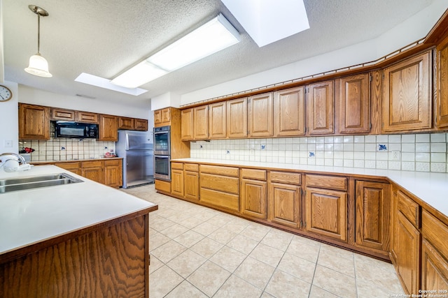 kitchen with brown cabinets, a sink, pendant lighting, light countertops, and appliances with stainless steel finishes