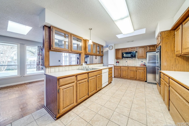 kitchen featuring appliances with stainless steel finishes, light countertops, a skylight, decorative light fixtures, and brown cabinetry