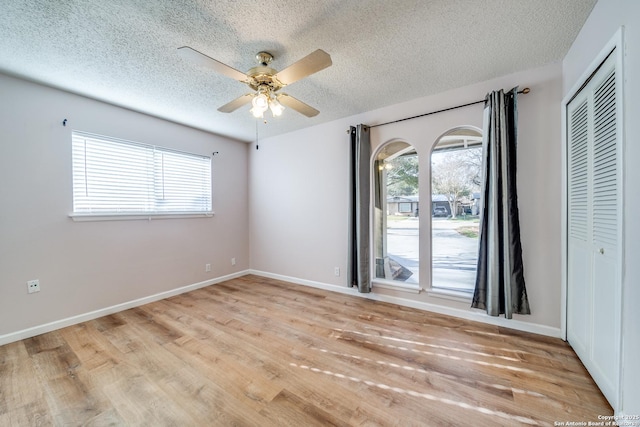 unfurnished room featuring a textured ceiling, light wood finished floors, a ceiling fan, and plenty of natural light