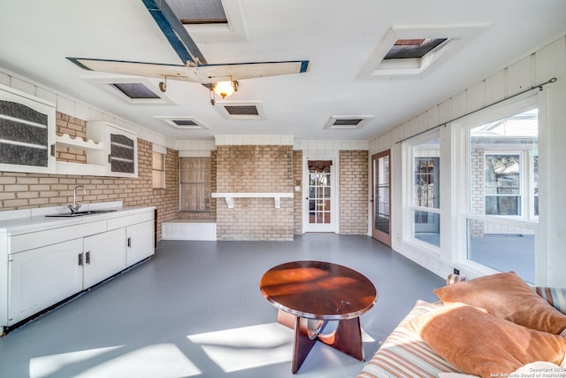 interior space featuring brick wall, finished concrete floors, white cabinetry, and a sink