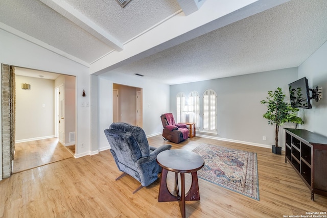 sitting room with light wood-style flooring, visible vents, baseboards, a textured ceiling, and lofted ceiling