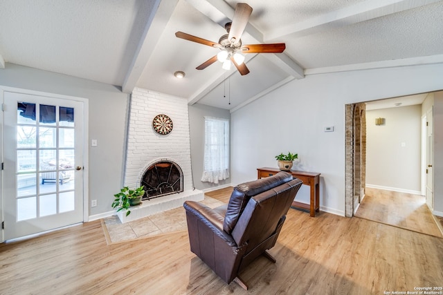 living room with a textured ceiling, a fireplace, light wood-type flooring, a wealth of natural light, and lofted ceiling with beams