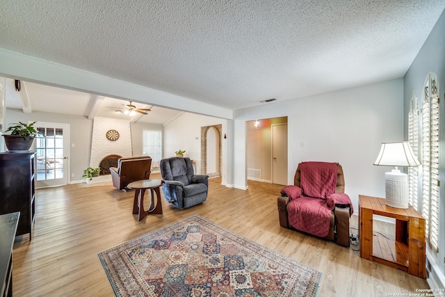 living area featuring light wood-style flooring, a textured ceiling, a brick fireplace, and beam ceiling