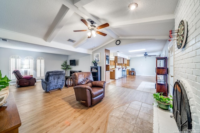 living room with lofted ceiling with beams, light wood-style flooring, visible vents, a brick fireplace, and a textured ceiling