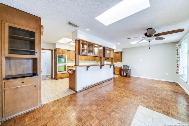 kitchen featuring visible vents, a skylight, glass insert cabinets, brown cabinetry, and a kitchen breakfast bar