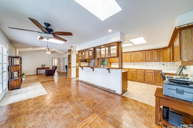 kitchen featuring vaulted ceiling with skylight, a breakfast bar, open floor plan, brown cabinets, and backsplash