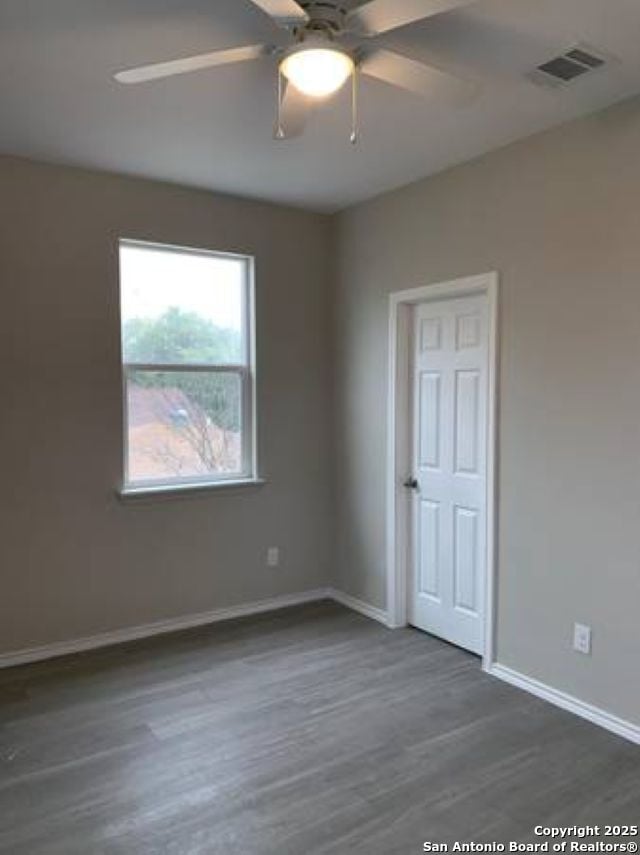 unfurnished room with ceiling fan, baseboards, visible vents, and dark wood finished floors