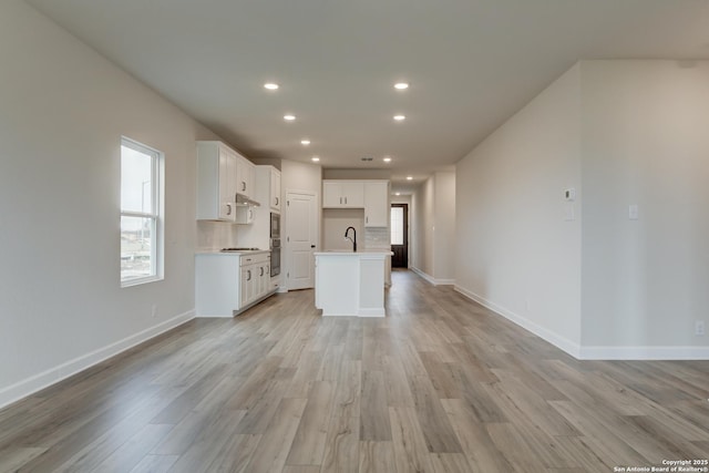 kitchen featuring an island with sink, white cabinetry, open floor plan, and light countertops