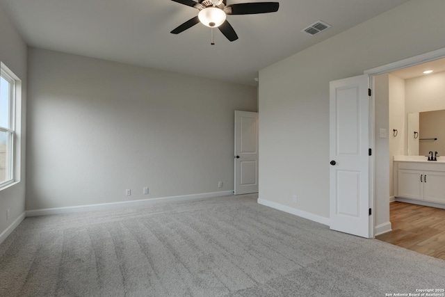 unfurnished bedroom featuring baseboards, visible vents, connected bathroom, light colored carpet, and a sink