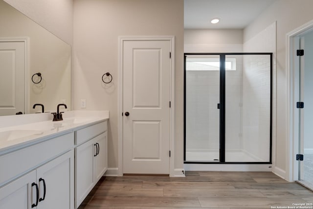 bathroom with double vanity, a stall shower, a sink, and wood finished floors