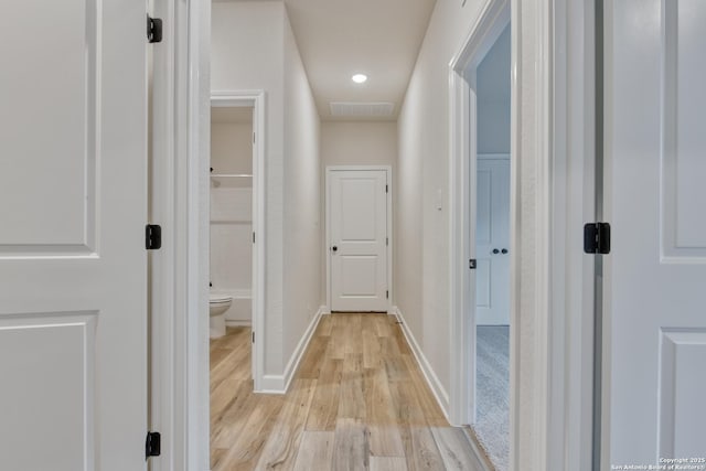 hallway with visible vents, light wood-style flooring, and baseboards